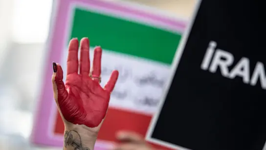 Eine rot bemalte Hand einer Demonstrantin erhebt sich zwischen Plakaten während einer Demonstration vor dem iranischen Konsulat in Istanbul. (Foto: Onur Dogman/SOPA/ZUMA/dpa)