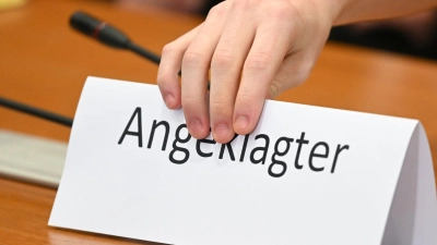 Ein Schild mit der Aufschrift „Angeklagter” wird auf die Gerichtsbank gestellt. (Foto: Arne Dedert/dpa/Symbolbild)