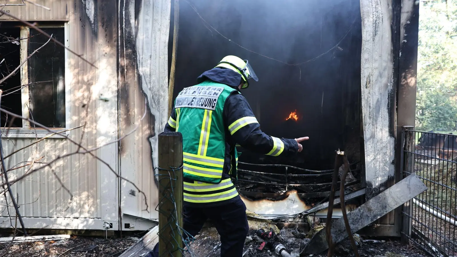 Ein Feuerwehrmann steht zwischen den qualmenden Trümmern einer Flüchtlingsunterkunft. (Foto: Daniel Karmann/dpa)