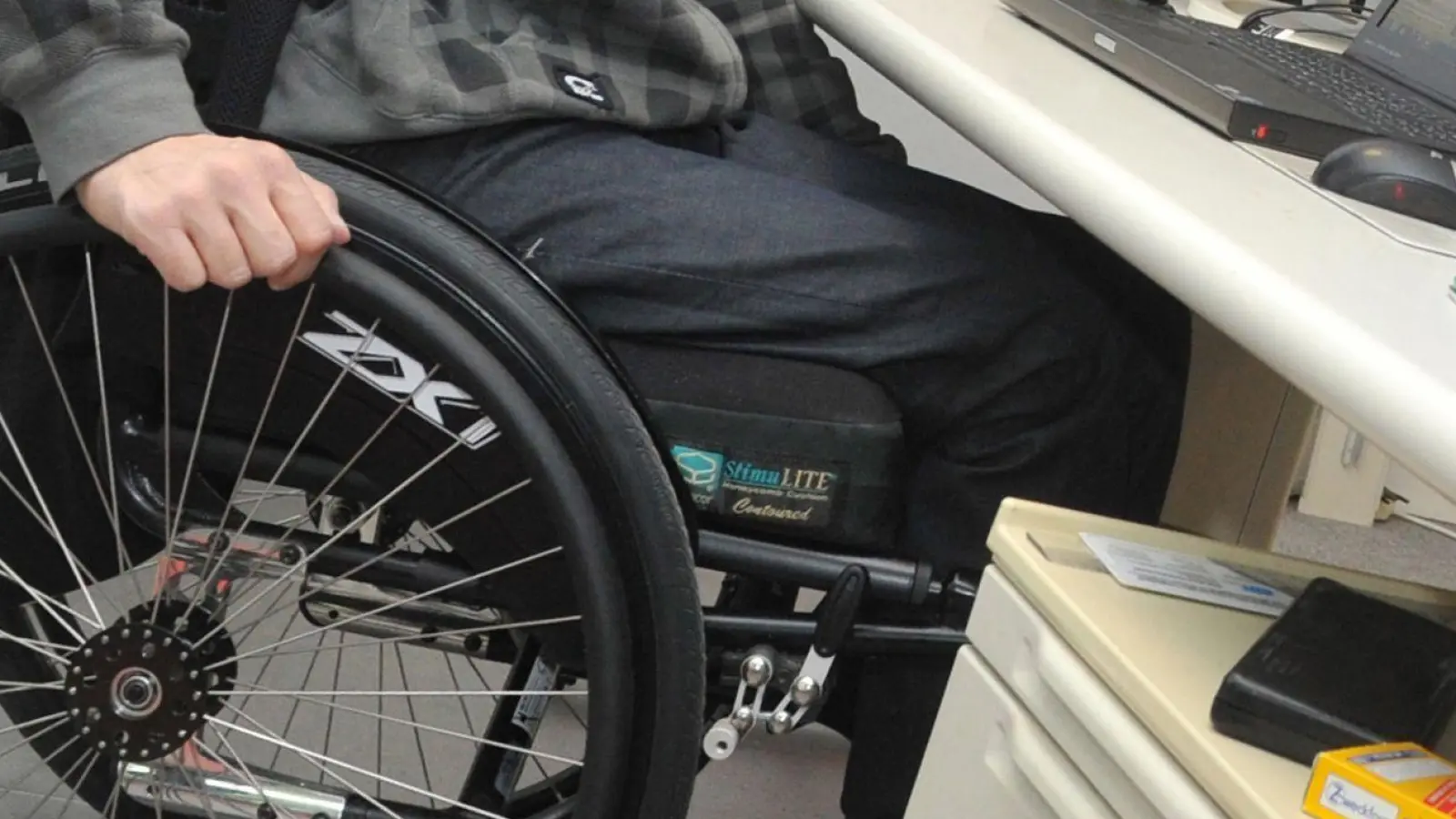Ein Mann sitzt in einem Rollstuhl an seinem Arbeitsplatz am Schreibtisch. (Foto: Stefan Puchner/dpa)
