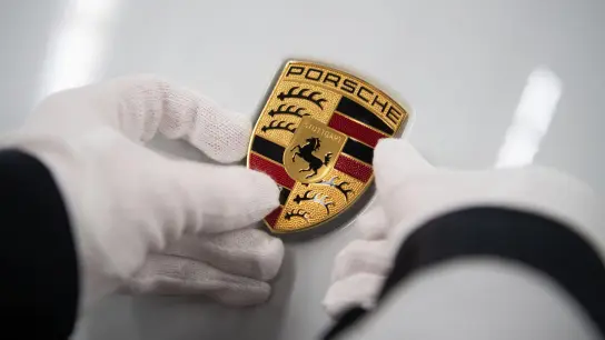 Eine Mitarbeiterin der Porsche AG hält in der Produktion ein Porsche-Emblem. (Foto: Marijan Murat/dpa/Archivbild)