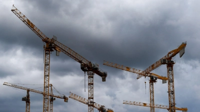 Dunkle Wolken ziehen über die Kräne auf einer Baustelle. „Alle Indikatoren am Bau zeigen deutlich nach unten, eine Trendwende ist nicht in Sicht“, stellt die Bauindustrie fest. (Foto: Lisa Ducret/dpa)