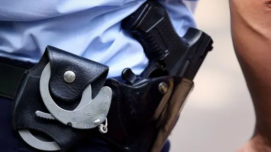 Ein Polizist trägt Handschellen und seine Dienstwaffe bei sich. (Foto: Oliver Berg/dpa/Symbolbild)