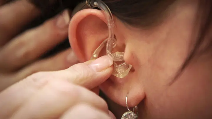 Eine Hörgeräteakustikerin setzt ein Hörgerät in das Ohr einer Hörgeschädigten. (Foto: picture alliance/dpa/Symbolbild)