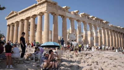Eine Touristin trinkt Wasser unter einem Sonnenschirm in der Hitze von Athen. (Foto: Petros Giannakouris/AP/dpa)