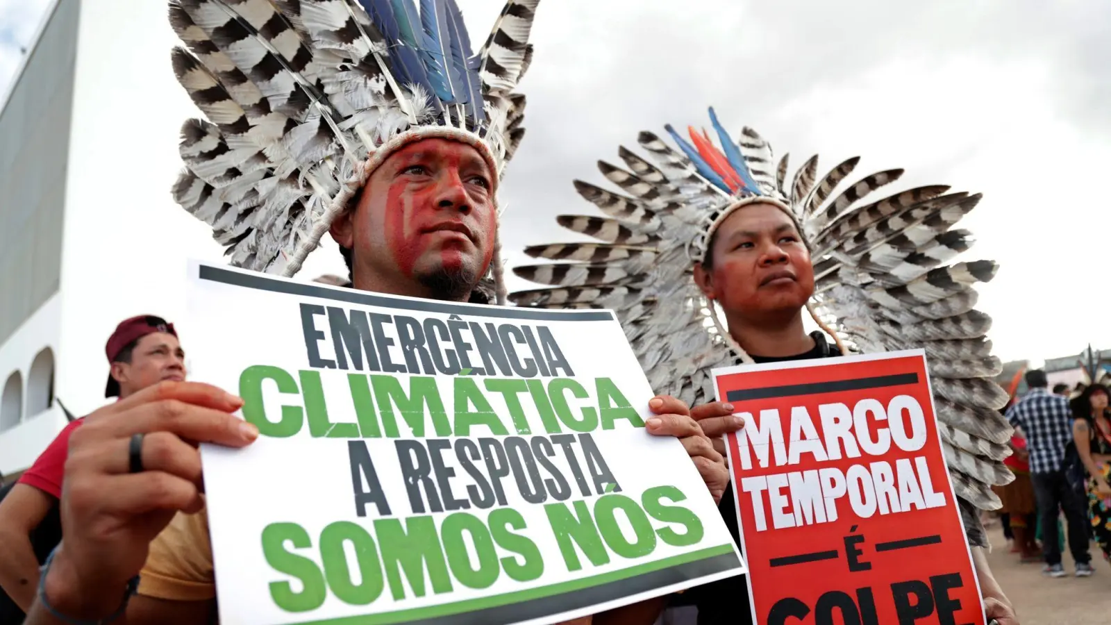 „Klima-Notstand - die Antwort sind wir“ steht auf dem Plakat (r) eines indigenen Demonstranten, der in Brasilia gegen den Gesetzesentwurf zur Ausweisung von Schutzgebieten protestiert. (Foto: Gustavo Moreno/AP)