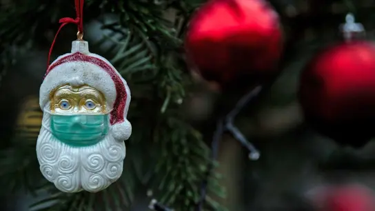 Ein Weihnachtsmann mit einer Schutzmaske hängt als Weihnachtsbaumschmuck in einem Tannenbaum. (Foto: Federico Gambarini/dpa)