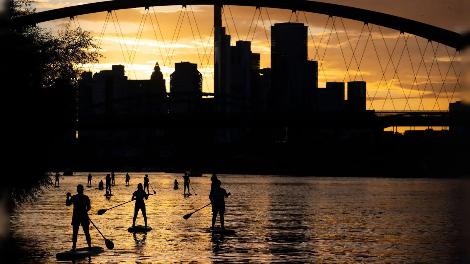 Bei Sicht auf die Skyline im letzten Licht des Tages fahren Stand-Up-Paddler in Nähe der Frankfurter Osthafenbrücke über den Main. (Foto: Boris Roessler/dpa)