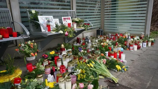 Kerzen und Blumen stehen und liegen im Bahnhof Brokstedt in einem Wartehäuschen. (Foto: Marcus Brandt/dpa)