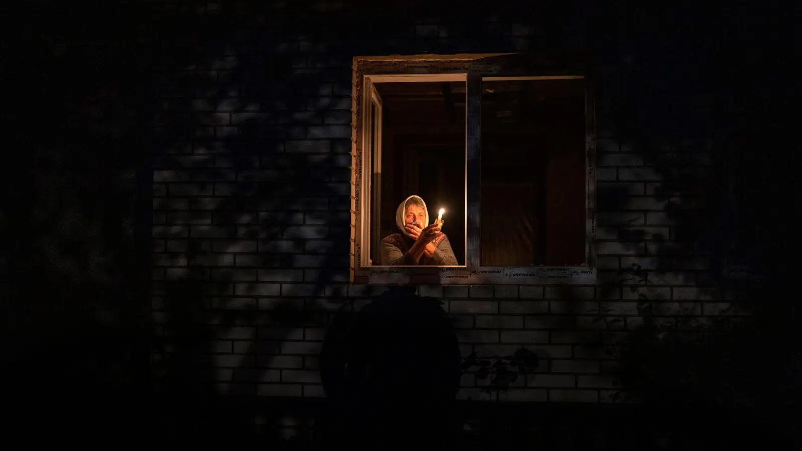 Die 70-Jährige Catherine steht während eines Stromausfalls in Borodjanka mit einer Kerze am Fenster. (Foto: Emilio Morenatti/AP/dpa)