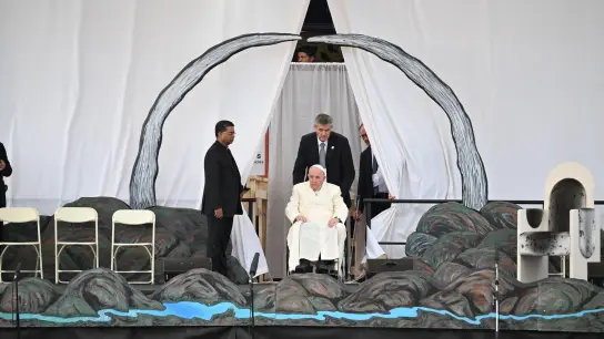 Papst Franziskus wird in seinem Rollstuhl auf die Bühne geschoben. (Foto: Johannes Neudecker/dpa)