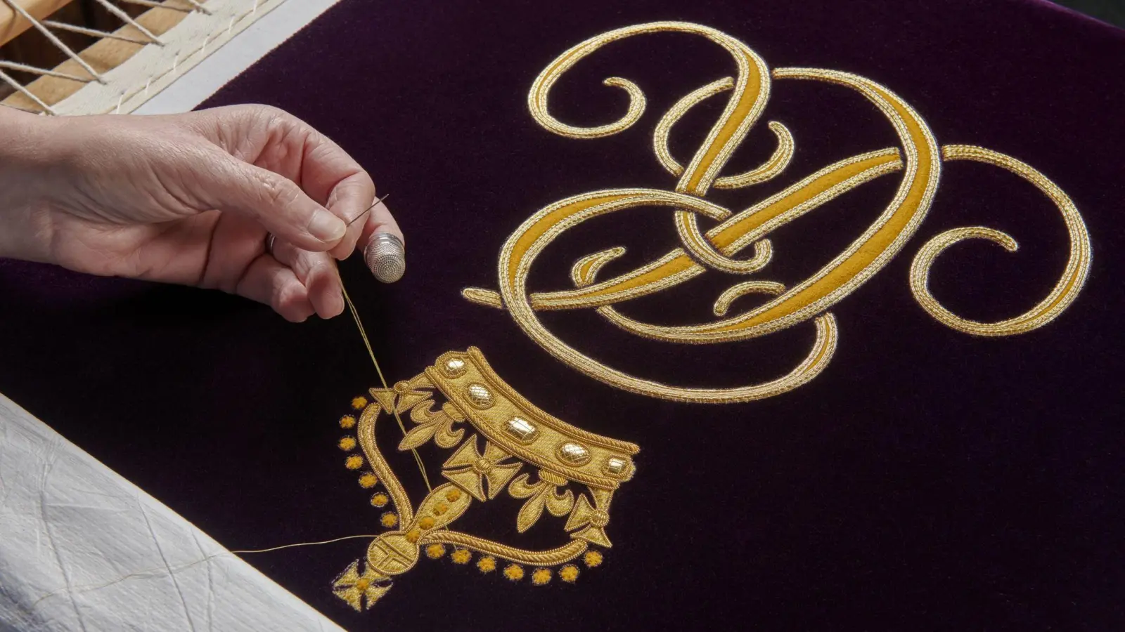 Ein Mitglied der Royal School of Needlework stickt den Schriftzug von Queen Camilla von Hand auf deren Robe. (Foto: Royal School Of Needlework/Buckingham Palace/PA Media/dpa)