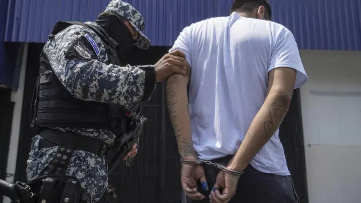 Ein vermummter Polizist in begleitet einen mutmaßlichen Mitglied einer Bande nach dessen Festnahme in San Salvador. (Foto: Camilo Freedman/dpa)