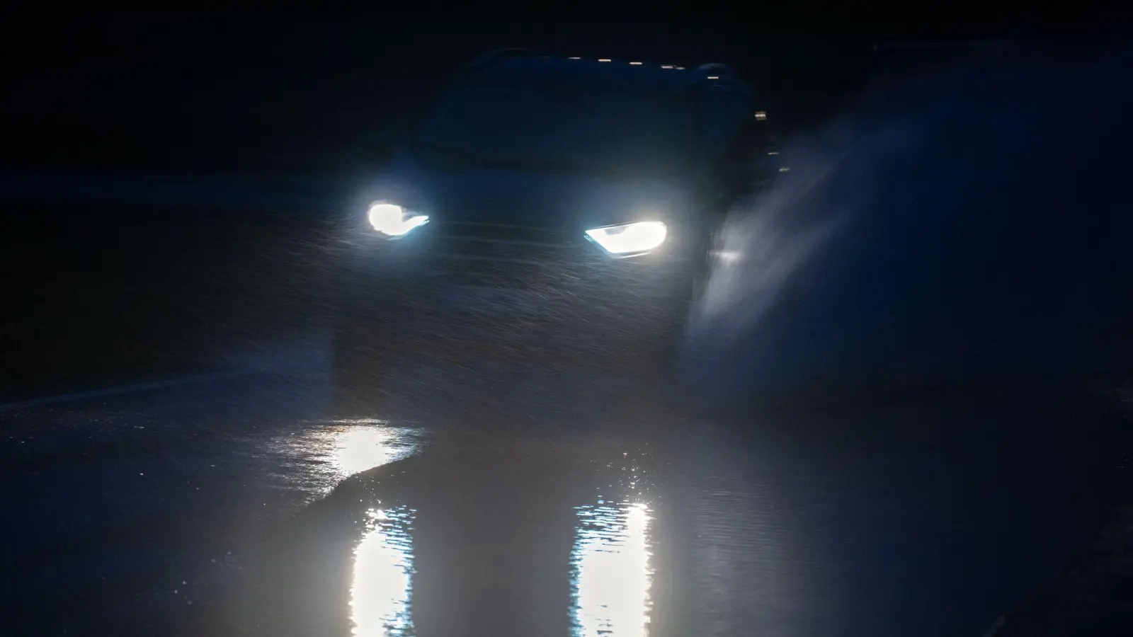 Wasser spritzt, während ein Auto über eine überschwemmte Straße zwischen Gleusdorf (Landkreis Haßberge, Unterfranken) und Busendorf (Landkreis Bamberg, Oberfranken) fährt. Im Itzgrund steigt das Hochwasser rasch an und es regnet weiter. Erste Straßen sind bereits gesperrt. (Foto: Pia Bayer/dpa)