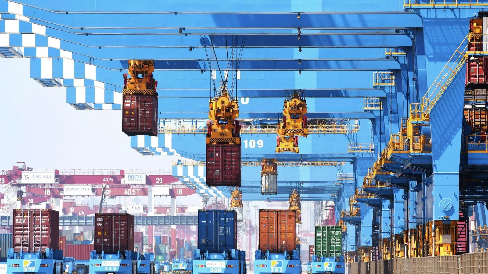 Portalkräne bewegen im Hafen von Qingdao im Osten Chinas Container auf Transporter. (Foto: Uncredited/CHINATOPIX/dpa)