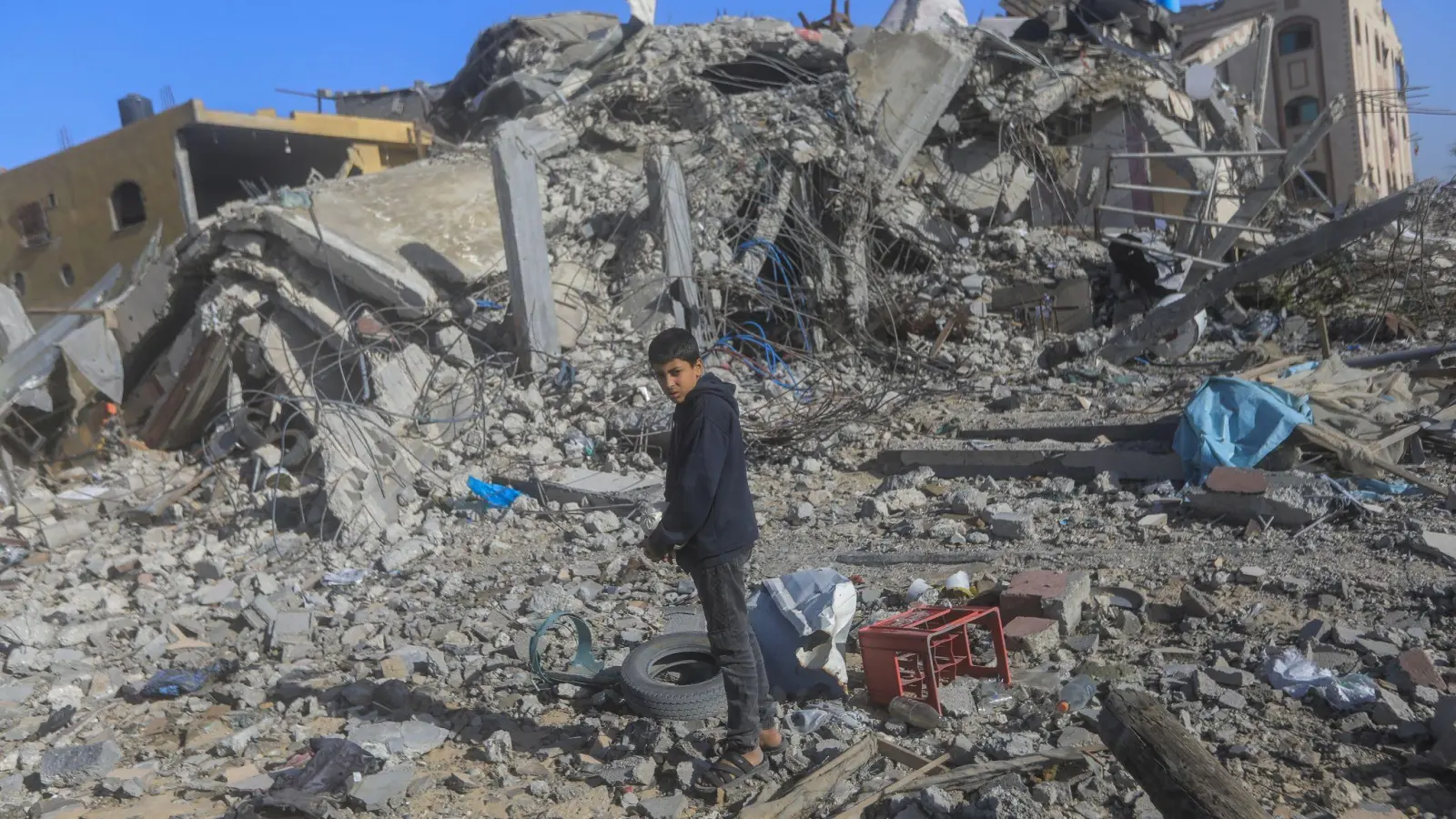 Ein junger Palästinenser auf den Trümmern von zerstörten Häusern nach israelischen Angriffen in Chan Juni im Gazastreifen. (Foto: Mohammed Talatene/dpa)