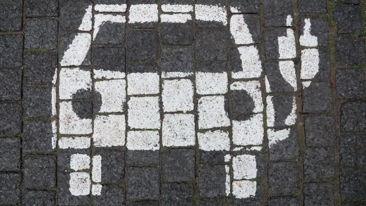 Ein Symbol markiert einen Parkplatz mit einer öffentlichen Ladesäule für Elektroautos. (Foto: Marco Rauch/dpa)