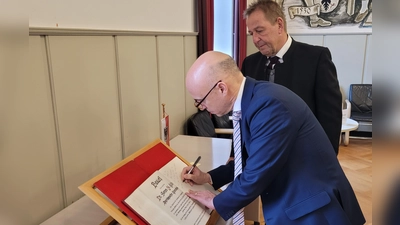 Der Generalkonsul Dr. James Miller (vorne) hat sich unter den Augen von drittem Bürgermeister Roland Reichenberg (hinten) ins Goldene Buch der Stadt Bad Windsheim eingetragen. (Foto: Nina Daebel)