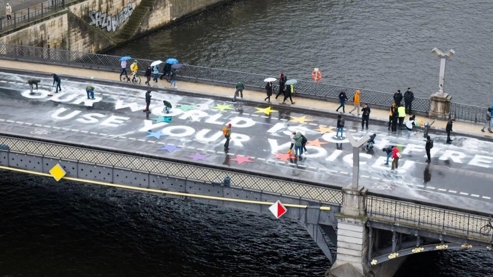 Klimaaktivisten der Bewegung Fridays for Future malen auf der Marschallbrücke in Berlin den Schriftzug „Our world is on fire - use your voice!“. (Foto: Christophe Gateau/dpa)