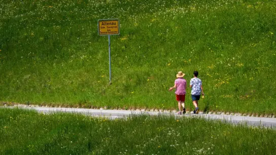 Ein Mann und eine Frau gehen auf einer Landstraße inmitten einer grünen Wiese spazieren. (Foto: Peter Kneffel/dpa)