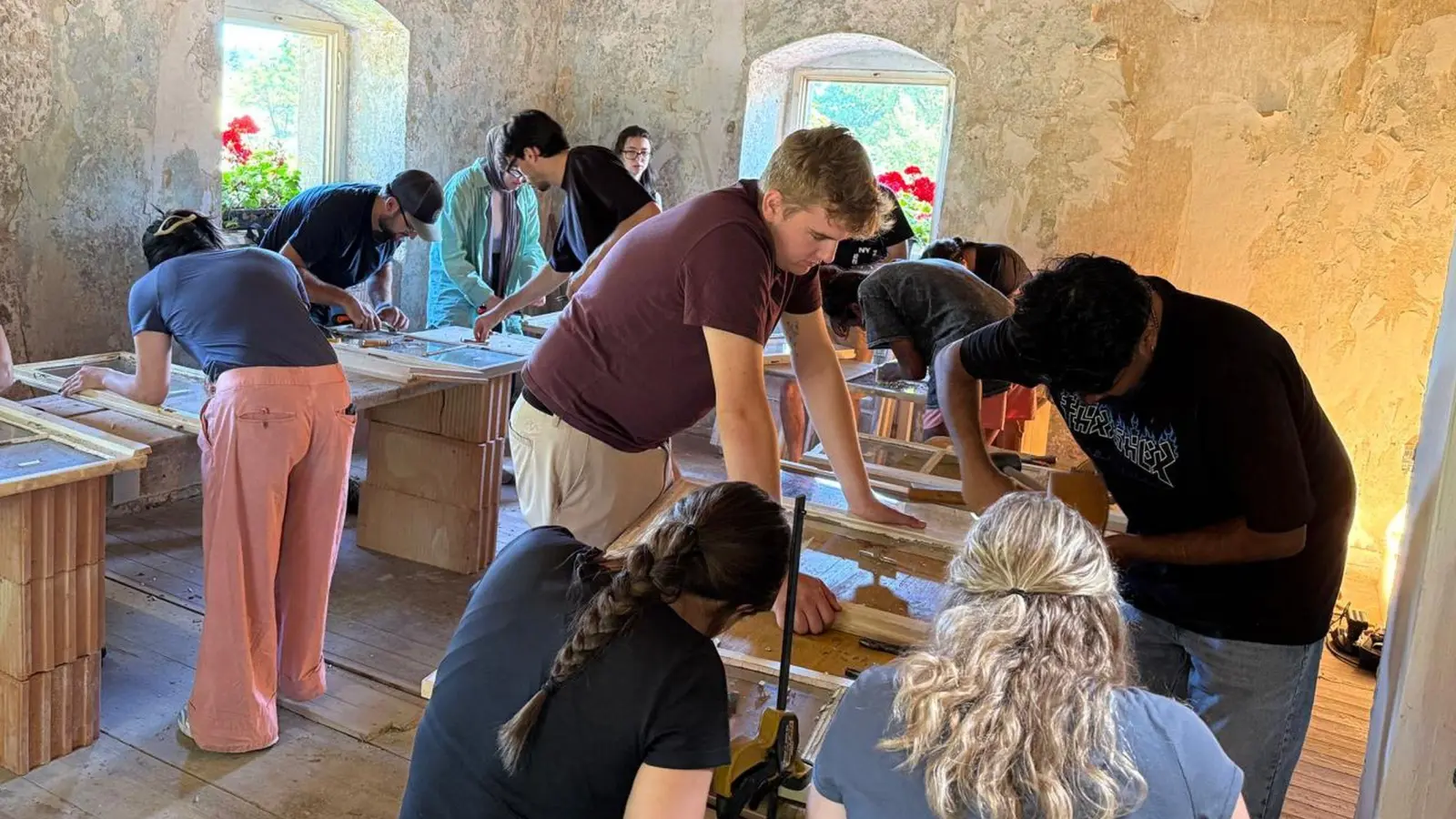 Aus Holzdielen und Ziegelsteinen haben sich die Studierenden aus Kanada im Parkwächterhaus Arbeitstische gebaut, auf denen die Fenster des Gebäudes zur Restaurierung liegen. Die jungen Leute ersetzen schadhafte Gläser und lassen das Holz mit Leinöl ein. (Foto: Randall Kober)