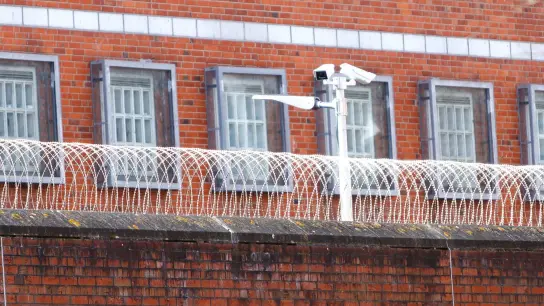 Eine Überwachungskamera steht hinter einem Stacheldrahtzaun der Justizvollzugsanstalt Neumünster. (Foto: Frank Molter/dpa)