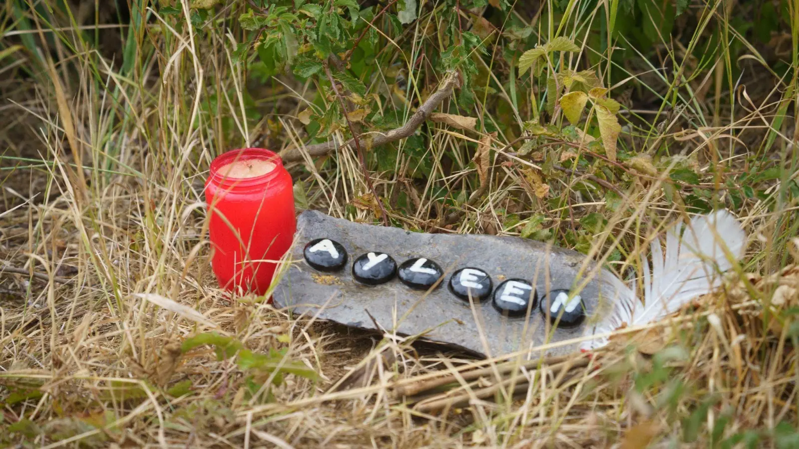 Eine Kerze und eine Tafel mit dem Namen Ayleen liegt am Ufer des Teufelsee im hessischen Wetteraukreis, wo die Leiche der 14-Jährigen  gefunden wurde. (Foto: Frank Rumpenhorst/dpa)