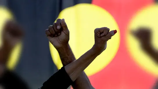 Ein Mann und eine Frau verschränken die Arme vor einer Aborigines-Flagge während einer Kundgebung der Bewegung „Black Lives Matter“ in Sydney (Symbolbild). Der „Sydney Morning Herald“ hat sich für seine Berichterstattung zum Myall-Creek-Massaker entschuldigt. (Foto: Rick Rycroft/AP/dpa)