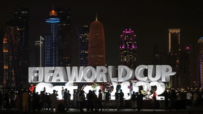 Menschen stehen vor der Eröffnung der WM vor einem beleuchteten Schriftzug „Fifa World Cup Qatar 2022“. (Foto: ---/kyodo/dpa)