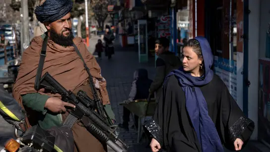 Eine Frau läuft in Kabul an einem bewaffneten Taliban-Kämpfer vorbei. Laut Amnesty International verschlechtert sich die Menschenrechtslage in Afghanistan rapide. (Foto: Ebrahim Noroozi/AP/dpa)
