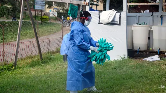 Ein Mitarbeiter in medizinischer Schutzkleidung trägt Schutzhandschuhe in einem Krankenhaus, in dem ein Ebola-Opfer isoliert wurde. (Foto: Ronald Kabuubi/AP/dpa)