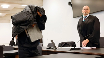 Der angeklagte Ex-Mitarbeiter eines Sicherheitsdienstes (l) bedeckt zu Prozessbeginn seinen Kopf mit einer Jacke. (Foto: Daniel Löb/dpa)