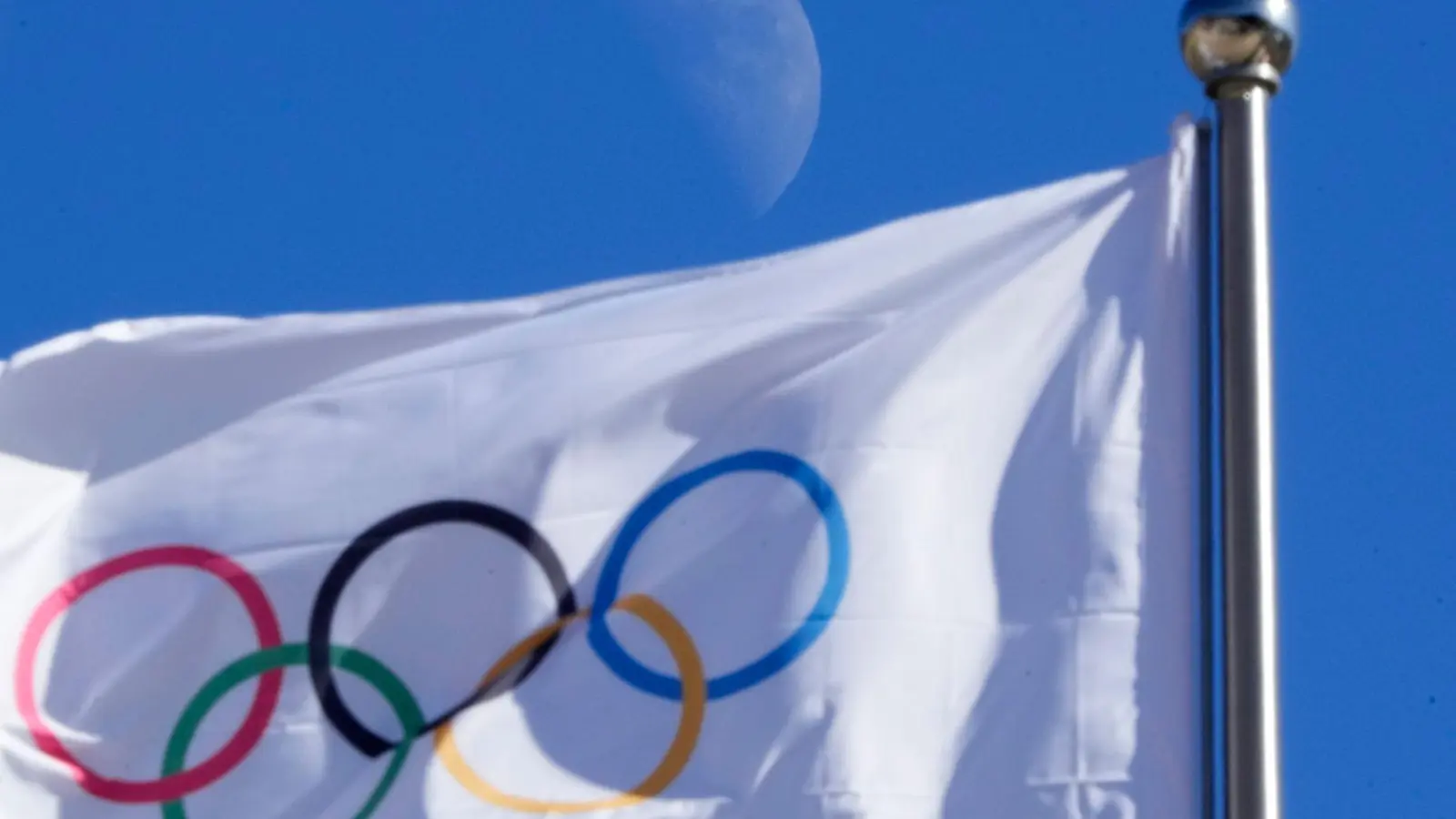 Eine olympischen Flagge weht vor blauem Himmel im Wind. (Foto: Dmitri Lovetsky/AP/dpa/Symbolbild)