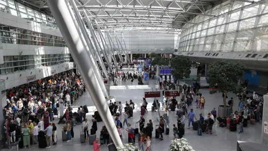Reisende stehen im Flughafen Düsseldorf in langen Warteschlangen an der Gepäckabgabe. (Foto: David Young/dpa)