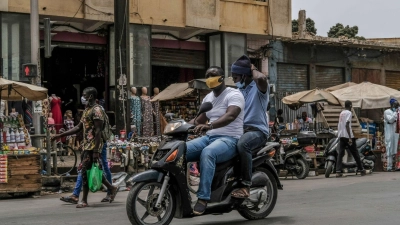 Mit Schutzmaske unterwegs auf dem Motorroller: Von der Risikoliste gestrichen wird unter anderem Senegal. (Foto: Eddy Peters/XinHua/dpa)