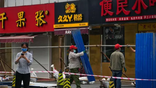 Arbeiter mit Gesichtsmasken stellen in Peking Metallbarrieren vor Einzelhandelsgeschäften und Restaurants auf, die im Rahmen von Covid-19-Maßnahmen geschlossen wurden. (Foto: Andy Wong/AP/dpa)