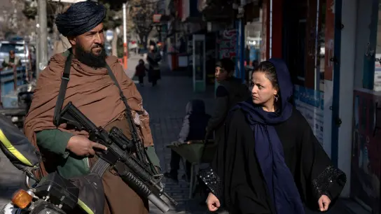 Eine junge Frau läuft in Kabul an einem Taliban-Kämpfer vorbei. (Foto: Ebrahim Noroozi/AP/dpa)