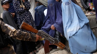 Ein Taliban-Kämpfer hält sein Gewehr in der Hand, während Menschen in Kabul auf die Verteilung von Lebensmittelrationen durch eine Hilfsorganisation warten. (Foto: Ebrahim Noroozi/AP/dpa)