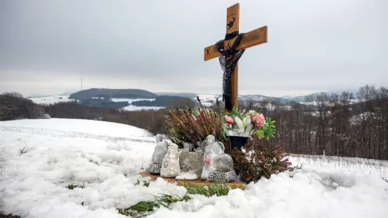 Ein Holzkreuz, Engelsfiguren und Blumen erinnern bei Kusel an die zwei Polizisten, die vor einem Jahr im Dienst getötet wurden. (Foto: Harald Tittel/dpa)
