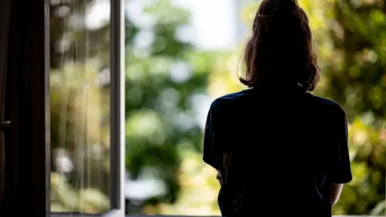 Eine Frau steht in ihrer Wohnung am Fenster. (Foto: Fabian Sommer/dpa/Illustration)