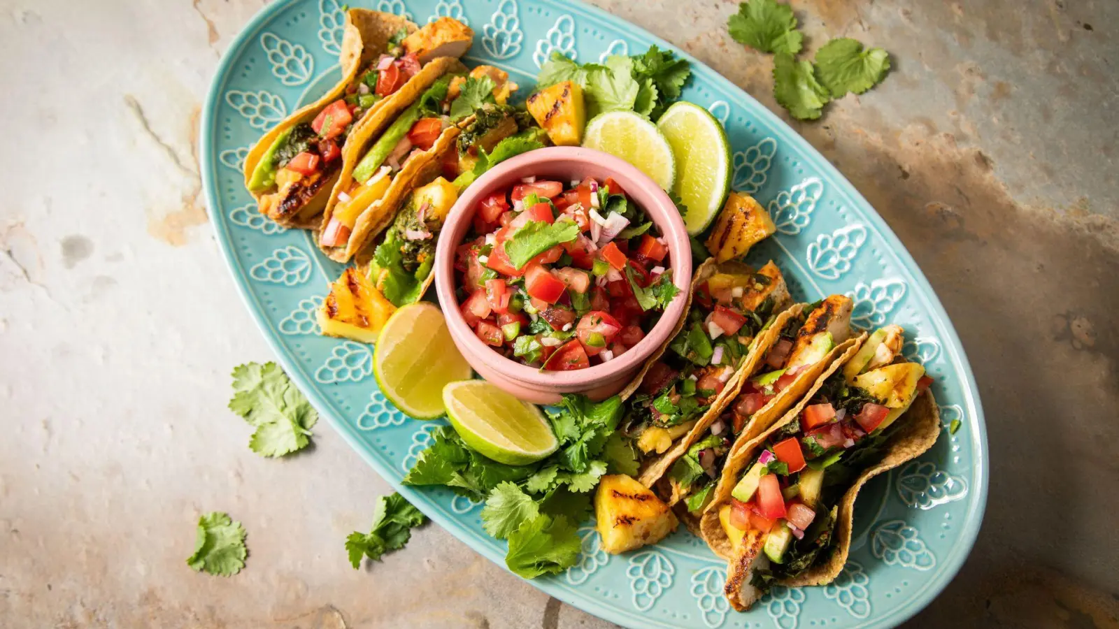Richtig stilecht werden Hähnchen-Tacos erst mit Zugaben wie der mexikanische Tomatensalsa „Pico de Gallo“, argentinischer Kräutersauce „Chimichurri“, Avocado, gegrillter Ananas, Koriander und Limetten. (Foto: Christin Klose/dpa-tmn)