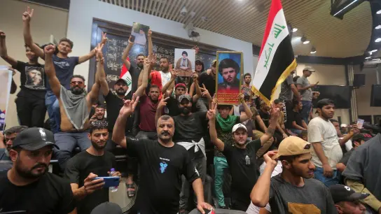 Irakische Demonstranten posieren mit Nationalflaggen und Bildern des schiitischen Geistlichen Al-Sadr vor dem Parlamentsgebäude. (Foto: Anmar Khalil/AP/dpa)
