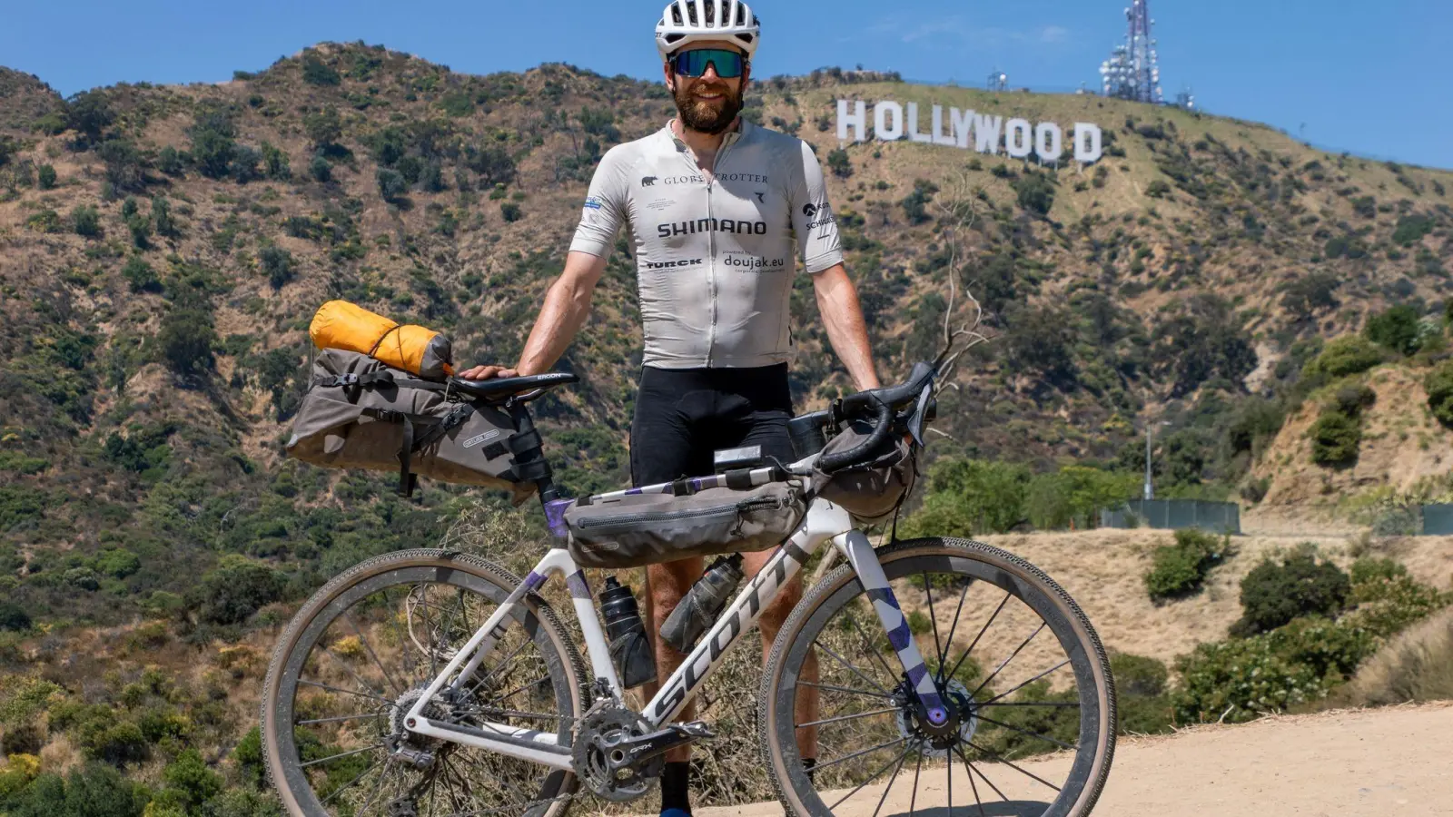 Der deutsche Athlet Jonas Deichmann mit seinem Fahrrad vor der Kulisse der Hollywood Hills in den USA. (Foto: Markus Weinberg/Jonas Deichmann/dpa)