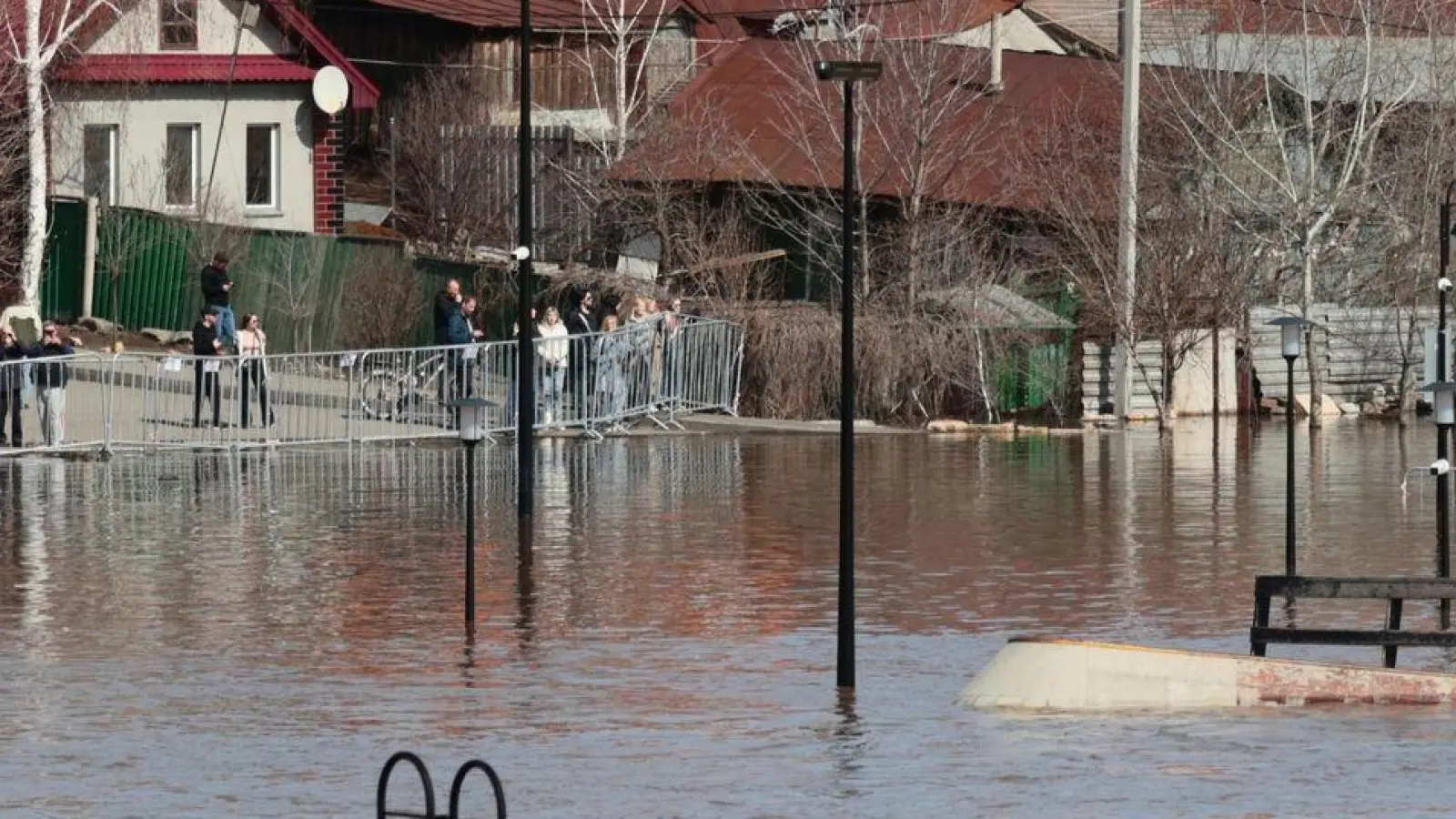 Anwohner stehen an einer Absperrung und beobachten ein überschwemmtes Gebiet im russischen Orenburg. (Foto: Uncredited/AP/dpa)
