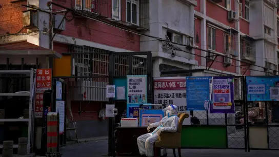 Ein Wachmann im Schutzanzug sitzt an einem Eingangstor zu einem Wohnviertel in Peking. (Foto: Andy Wong/AP/dpa)