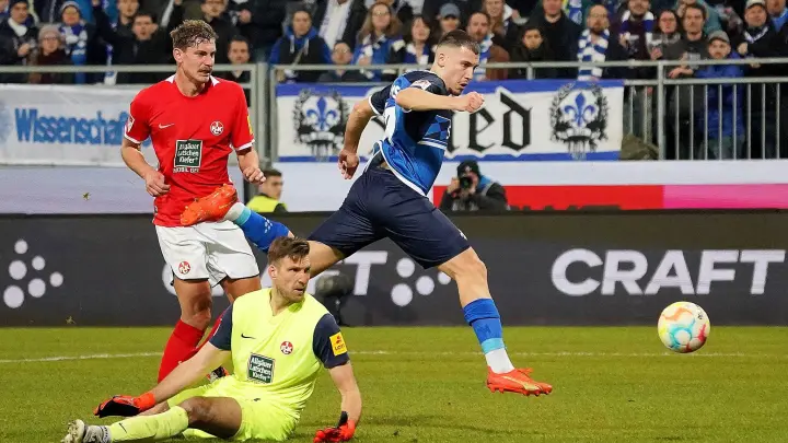 Darmstadts Filip Stojilkovic (r) erzielt den Treffer zum 2:0. Kaiserslauterns Kevin Kraus (l) und Torwart Andreas Luthe (M) schauen hinterher. (Foto: Hasan Bratic/dpa)