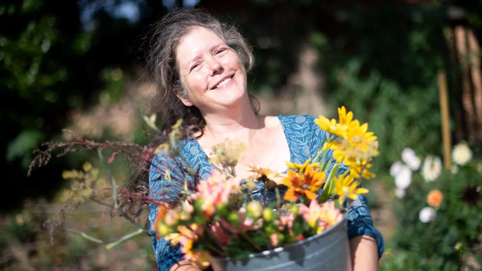 Claudia Werner steht mit einem Eimer mit frisch geschnittenen Blumen in ihrem Garten. Früher arbeitete die Bremerin als Erzieherin - heute hat sie eine eigene Gärtnerei. (Foto: Sina Schuldt/dpa)