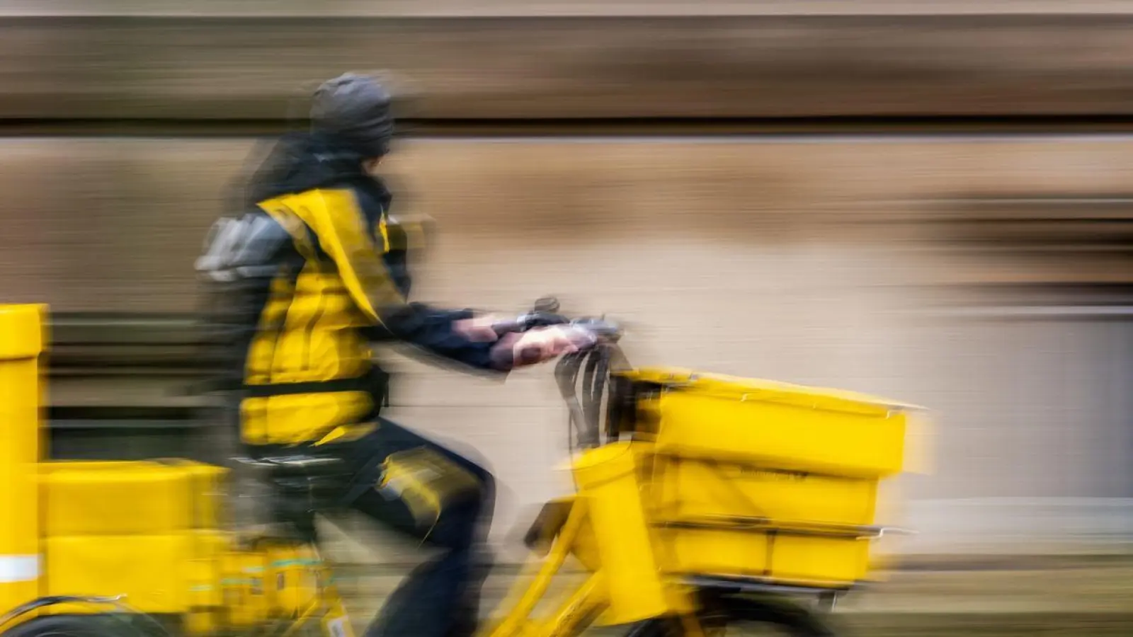 Ein Postbote der Deutschen Post fährt auf einem Lastenrad auf einem Gehweg entlang. (Foto: Robert Michael/dpa/Symbolbild)