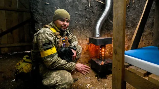 Ein ukrainischer Soldat wärmt sich an einem Ofen. (Foto: ---/Ukrinform/dpa)