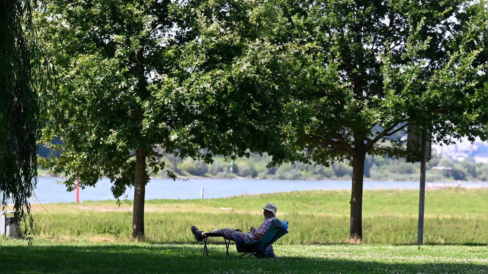 Ein Mann hat sich ein schattiges Plätzchen am Ufer des Rheins in Leverkusen gesucht. (Archivbild) (Foto: Roberto Pfeil/dpa)